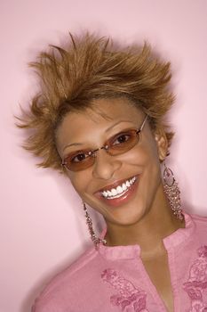 Portrait of smiling young African-American adult woman on pink background wearing sunglasses.