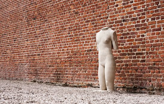 Lonely sculpture standing next to red-brick wall