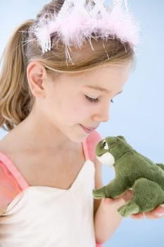 Young girl in princess costume kissing plush frog