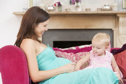 Pregnant mother with daughter in living room touching belly 
