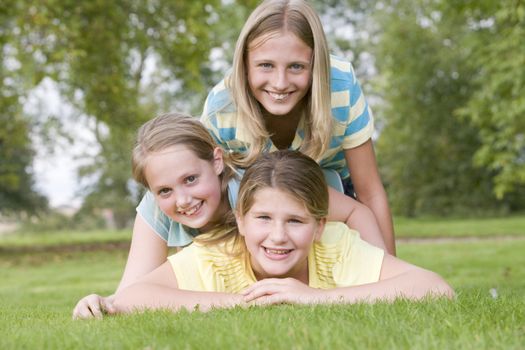 Three young girl friends piled on each other outdoors smiling