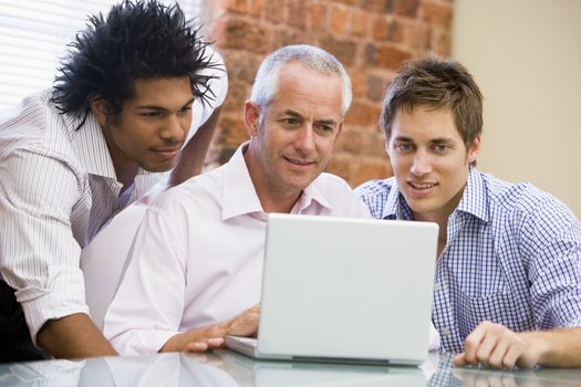Three businessmen in office looking at laptop smiling