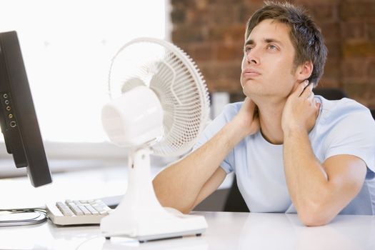Businessman in office with computer and fan cooling off