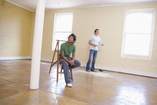 Two men in empty space with ladder holding paper