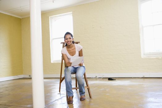Woman sitting on ladder in empty space holding paper smiling