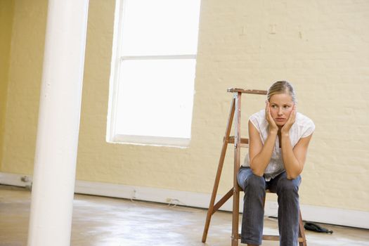 Woman sitting on ladder in empty space looking bored
