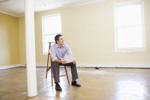 Man sitting on ladder in empty space holding paper