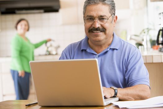 Man in kitchen with laptop smiling with woman in background