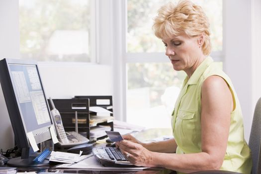 Woman in home office at computer with credit card frowning