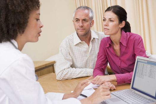 Doctor with laptop and couple in doctor's office frowning