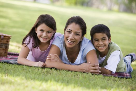 Mother and two young children outdoors in park with picnic smiling