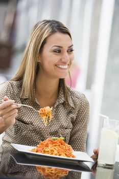 Woman at restaurant eating spaghetti and smiling