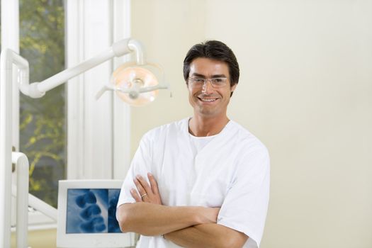 dentist with arms folded smiling and standing in his office