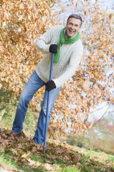 Man outdoors raking leaves and smiling 
