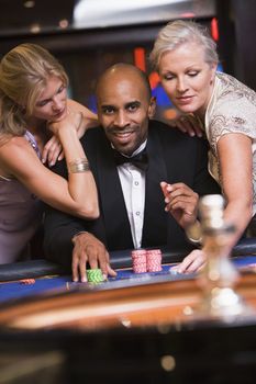 Three people in casino playing roulette smiling