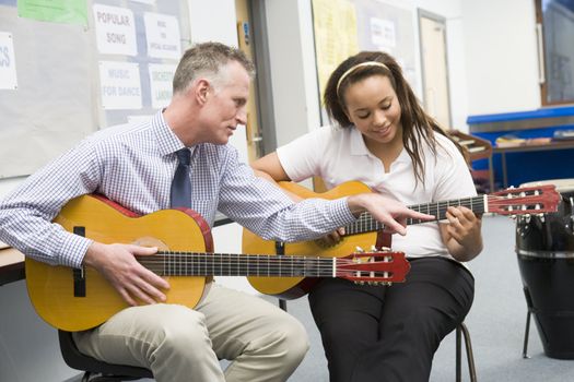 Female student receiving guitar lesson from teacher in classroom 