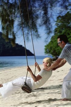 Man outdoors by a beach pushing a woman on a swing (selective focus) 