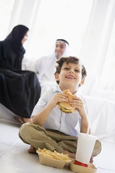 Young boy with fast food in living room with parents in background (high key/selective focus) 