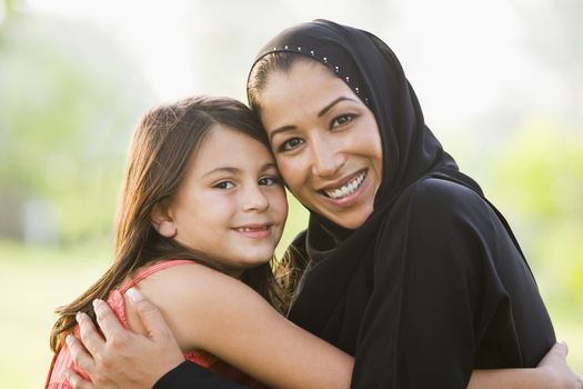 Mother and daughter outdoors in park embracing and smiling (selective focus) 