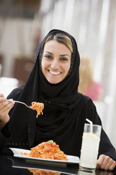 Woman at restaurant eating spaghetti and smiling (selective focus) 