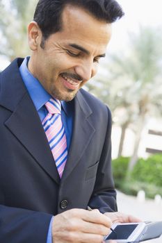 Businessman outdoors using personal digital assistant and smiling (high key/selective focus) 