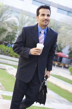 Businessman walking outdoors with coffee smiling (high key/selective focus) 