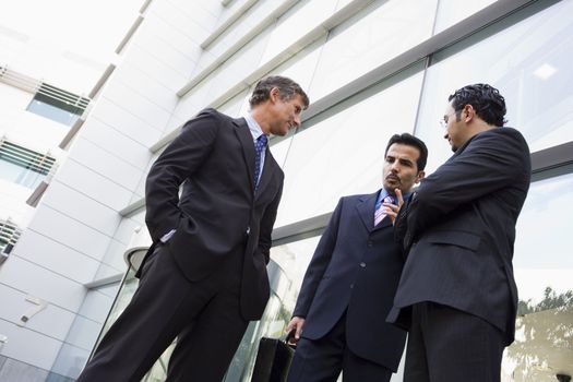 Three businessmen standing outdoors by building talking (high key/selective focus) 