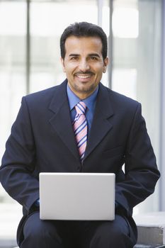 Businessman sitting outdoors by building with a laptop (high key/selective focus) 