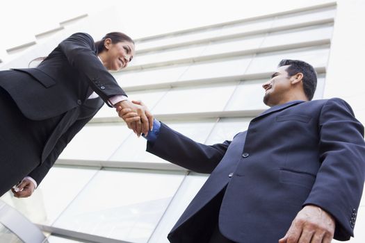 Two businesspeople outdoors by building shaking hands and smiling (high key/selective focus) 