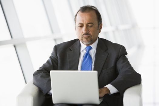 Businessman sitting indoors with laptop (high key/selective focus) 