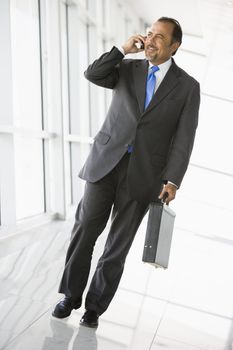 Businessman walking in corridor on cellular phone smiling (high key/selective focus)