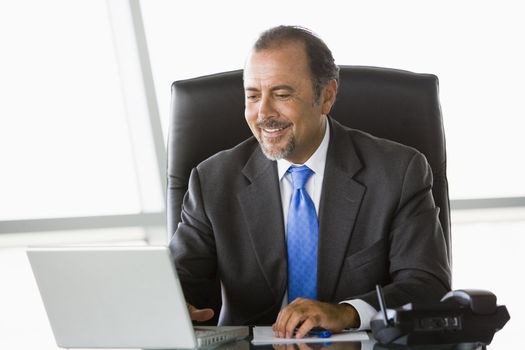 Businessman in office with laptop smiling (high key/selective focus) 