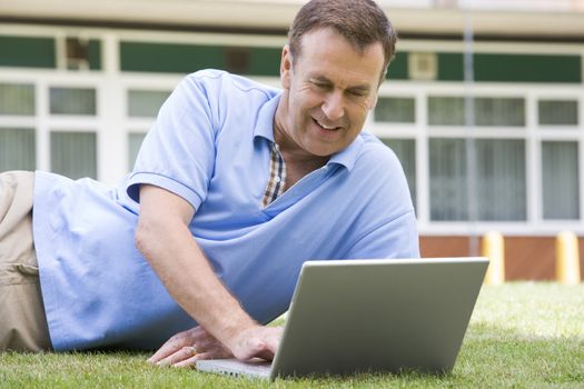 Man lying on lawn of school with laptop