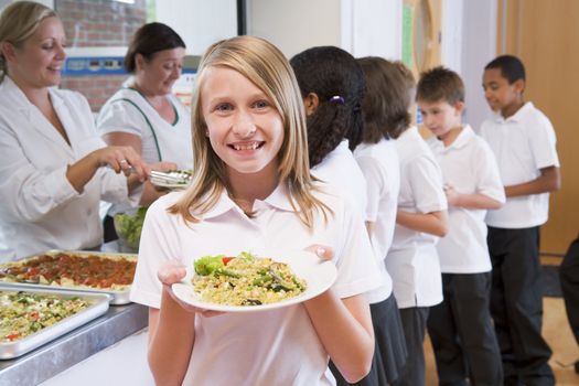 Students in cafeteria line with one holding up her healthy meal and looking at camera (depth of field)