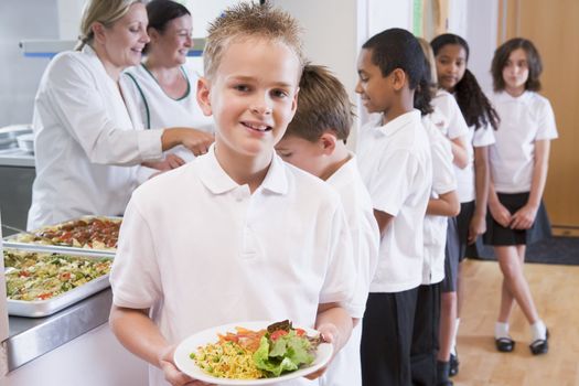 Students in cafeteria line with one holding his healthy meal and looking at camera (depth of field)