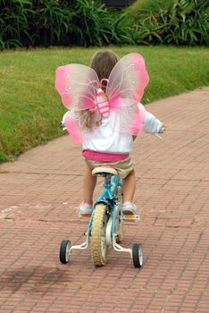 Little girl under butterfly costume wings riding a bike in a park