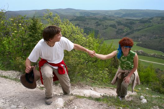 tourist man helping woman climb on the mountain