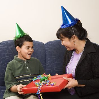 Mother giving present to surprised son at birthday party.