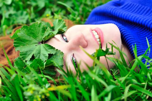 face of redheaded girl laying on the green grass with crown from leaves
