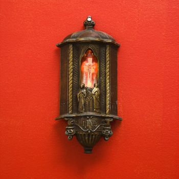 Religious light on red wall with illuminated Crucifixion of Jesus on cross.