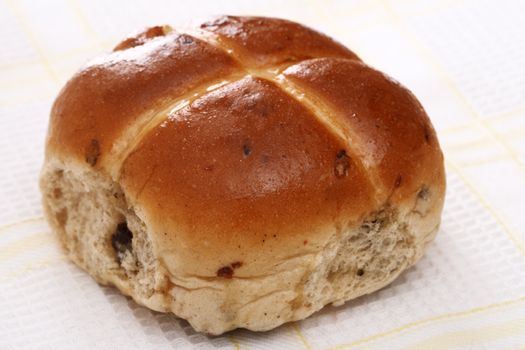 hot cross bun with currant on a tea-cloth background