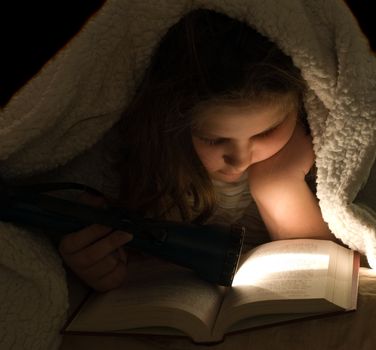 Closeup view of a young girl reading a book in the dark, with a flashlight