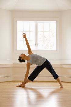 Young woman doing yoga triangle pose indoors by sunlit window.