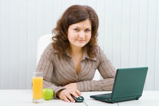 Young smiling woman with a laptop and juice sits in the office
