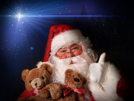 Santa smiling holding toy teddy bears in his arms aginst a night sky