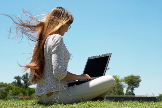Happy young girl smiling and working on a laptop outdoors