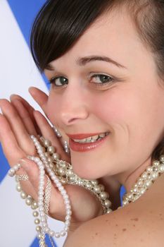 Beautiful brunette female holding pearl jewellery against Scottish flag