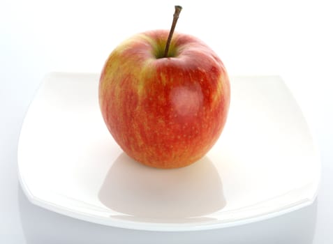 The ripe red apple lays on a white plate
