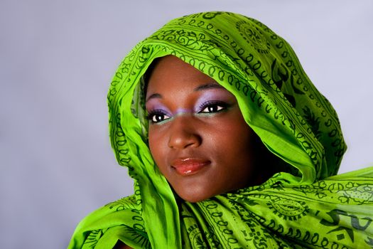 The face of an innocent beautiful young African-American woman with green headwrap and purple-green makeup, isolated