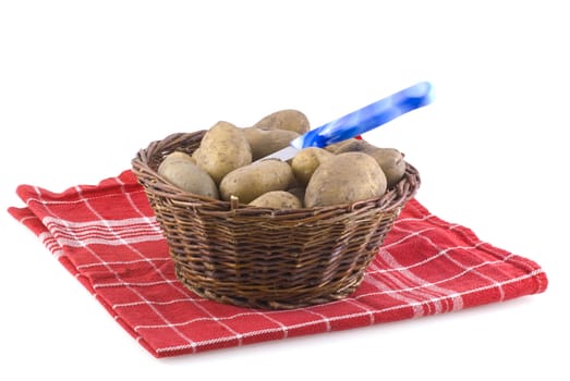 Basket full of potatoes with knife, standing on cloth, isolated on white.